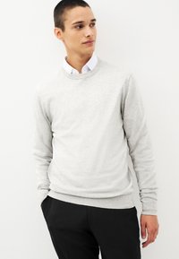 Pull gris clair en matériau doux avec un col rond et des poignets côtelés. Assorti avec un pantalon noir, créant un look monochrome harmonieux.