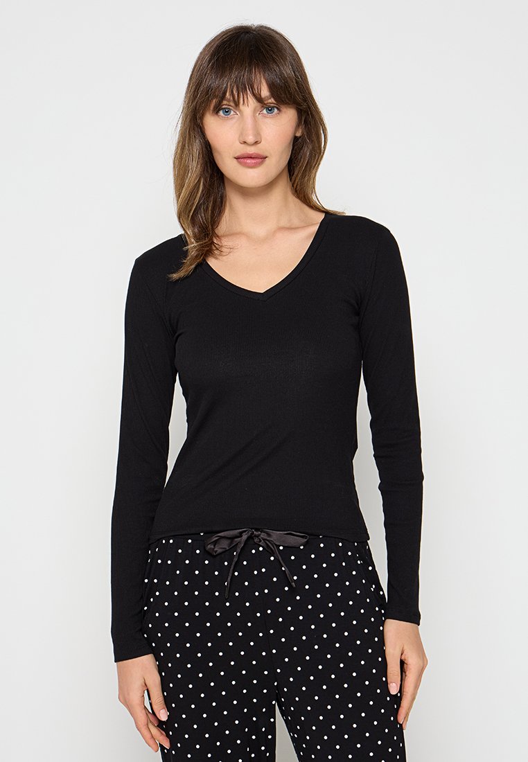 Czarna bluzka z długim rękawem i dekoltem w serek, wykonana z prążkowanej tkaniny, zestawiona z czarnymi spodniami w kropki i elastycznym ściągaczem w pasie. Prosty i dopasowany krój.