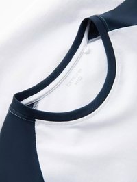 Kortærmet skjorte med hvid krop og marineblå detaljer på ærmerne og halsudskæringen. Stoffet ser glat ud med et rundt kravedesign.