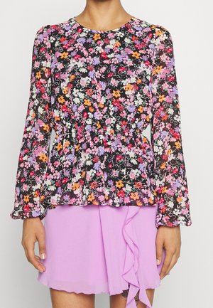 Blusa floral de manga larga, con fondo negro, flores coloridas y cintura peplum. Combinada con una falda lila con volantes.