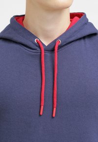 Felpa blu navy con fodera rossa, dotata di occhielli in argento e lacci rossi. Texture morbida e design casual.