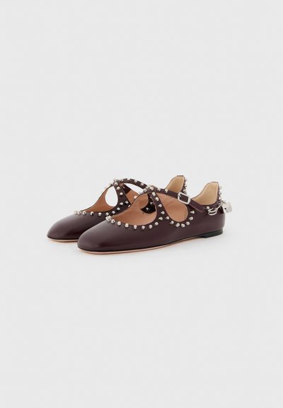 Chaussures en cuir bourgogne avec un design découpé, ornées de clous métalliques le long des bords, dotées d'une bride de cheville réglable et d'une semelle plate.