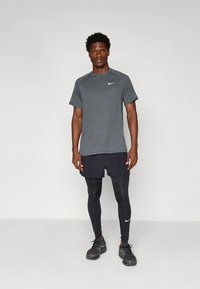 Nike sportöltözet sötétszürke, texturált rövid ujjú pólóval, fekete rövidnadrággal és fekete leggingsszel, fekete futócipővel kiegészítve.