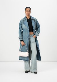 Denim trench coat med snittet krage, lysvasket og slitte detaljer, båret over en svart kortermet genser og lett utsvungne jeans.