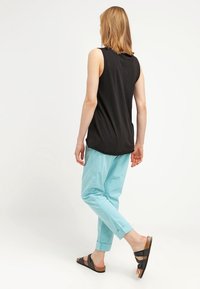 Svart ärmlös topp och ljusblå tapered byxor med avslappnad passform. Modellen har på sig svarta sandaler, vilket visar en enkel, avslappnad stil.