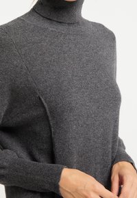 Maglione grigio a collo alto realizzato in un tessuto morbido e leggero. Presenta polsini a costine e una trama sottile. Silhouette elegante e aderente.