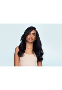 Lang, glanzend zwart haar in zachte golven gestyled, gedragen met een lichtbeige mouwloze top tegen een lichtblauwe achtergrond.
