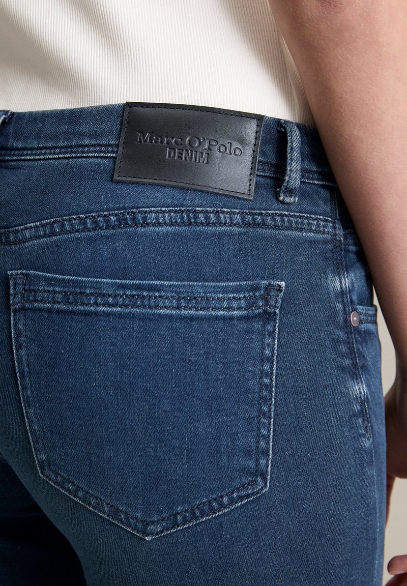 Dunkelblaue Denim-Jeans verfügen über ein Lederpatch mit der Aufschrift "Marc O'Polo DENIM" auf der Rückseite, haben ein klassisches Fünf-Taschen-Design und eine subtile Textur.