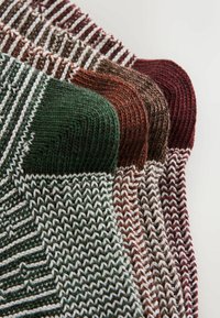 Adīti šalliņi zaļos, brūnos un burgundijas toņos, ar teksturētām svītrām un kontrastējošām baltām līnijām gar malām.