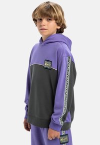 Haut à capuche violet et gris avec une poche frontale, un cordon de serrage pour la capuche et des accents latéraux estampillés. Le tissu semble doux avec une coupe décontractée.