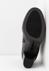 Zwarte leren schoen met een lage hak. De rubberen buitenzool heeft een geribbeld patroon. Zijkanten zijn voorzien van stiksels en een logolabel.