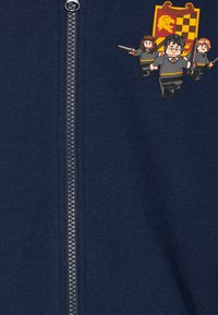 Jūrinio stiliaus zip-up džemperis su priekyje esančia užtrauktuku ir LEGO personažų dizainais. Su Gryffindor herbu ir detaliu audinio apdorojimu.