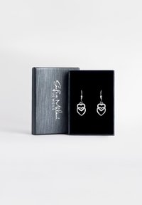 Orecchini a forma di cuore in argento esposti in una scatola foderata in velluto nero con un rivestimento esterno in argento testurizzato. Design elegante a cerchio con accentuazioni.