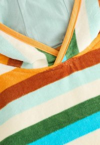 Un material cu dungi multicolore în nuanțe de albastru deschis, verde, marron, portocaliu și crema; cu o textură moale, plăcută la atingere și având un design cu guler în V.