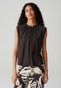 Top senza maniche nero con scollatura arricciata, in tessuto misto cotone, abbinato a pantaloni a fantasia con grandi disegni astratti bianchi.