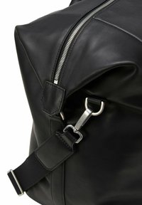 Sac en cuir noir avec une fermeture éclair argentée et un clip métallique sur la bandoulière. Texture lisse avec un design plié, mettant en avant son esthétique minimaliste.