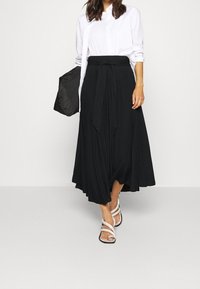 Mustas, virvantev maxi seelik, millel on seotud talje detail, koos valge nööpidega särgiga ja valgete rihmadega sandaalidega.