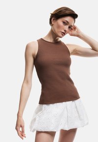 Top sin mangas de canalé marrón con un cuello alto, combinado con una falda blanca de tejido de ojal con recortes florales. Textura suave y diseño ajustado.