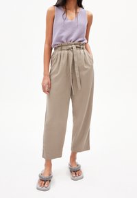 Světle fialová bezrukávová košile s výstřihem do V, spárovaná s béžovými kalhotami s vysokým pasem a páskem. Šedé sandály s propleteným vzorem na podrážkách.