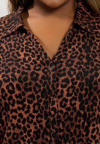 Camicia con stampa leopardata in ruggine e nero, caratterizzata da un tessuto testurizzato, colletto e chiusura con bottoni. Motivo animale distintivo su tutta la superficie.