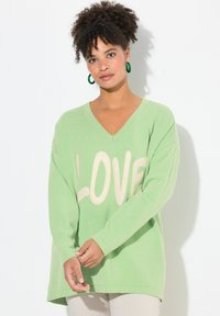 Maglione lavorato a maglia verde chiaro con scollo a V, con la scritta "LOVE" in lettere crema sulla parte anteriore. Vestibilità ampia con maniche lunghe.