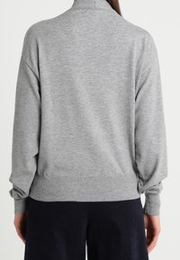 Pull en gris à col haut, manches raglan et bords côtes aux poignets et à l'ourlet. Texture lisse, coupe décontractée.