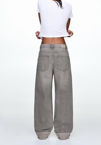 Jean en denim gris à jambes larges, taille haute et design à cinq poches. Le tissu présente une texture subtile et une finition propre et minimaliste.