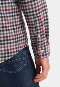 Camicia a quadri rossa, bianca e blu navy, in tessuto morbido, con maniche lunghe, caratterizzata da bottoni bianchi ai polsini e un orlo arrotondato.