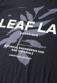 Sort stof med stort gråt bladgrafik og hvid tekst, inklusive "LEAF," "BOTANIQUE," og "BOTANICAL ENGINEERING AND RAW MATERIALS."