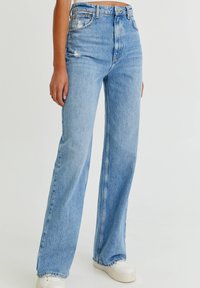 Jeans de denim azul claro con una cintura alta, pierna ancha y detalles desgastados. Presenta un clásico diseño de cinco bolsillos y un ligero desvanecimiento.