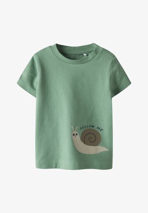 Camiseta de algodón verde de manga corta con una ilustración de un caracol y el texto "SÍGUEME" en negro. Textura suave, ajuste estándar.