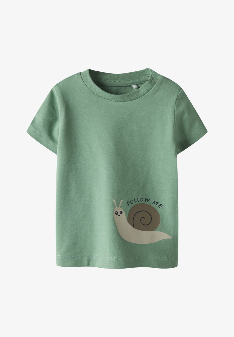 Camiseta de algodón verde de manga corta con una ilustración de un caracol y el texto "SÍGUEME" en negro. Textura suave, ajuste estándar.