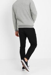 Felpa grigia trapuntata con scollatura rotonda, abbinata a pantaloni neri a gamba affusolata e sneakers scure con accenti bianchi.