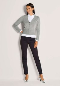 Grauer V-Ausschnitt-Cardigan mit Knöpfen, getragen über einem weißen Hemd mit Kragen, kombiniert mit schwarzen Slim-Fit-Hosen und silbernen High Heels.