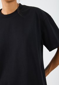 T-shirt noir en coton avec un col rond classique, des manches courtes et une coupe décontractée, d'une texture lisse et sans motifs visibles.