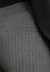 Material herringbone gri cu dungi fine, pantaloni croiți cu un buzunar posterior și un material negru neted deasupra taliei.