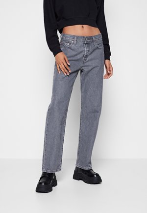 Vrouw draagt high-waist grijze rechte jeans, zwarte cropped sweatshirt en zwarte chunky platform schoenen, staand tegen een witte achtergrond.