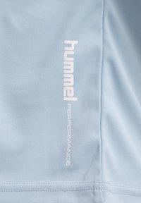 Ljusblå atletisk skjorta med en texturerad tyg och en vertikal vit logotyp som står "hummel PERFORMANCE" på vänster sida.