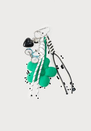 Porte-clés avec fleur en tissu verte, breloque vélo bleue, cœur noir, cœur métallique, cordons noirs et blancs attachés à un clip argenté.