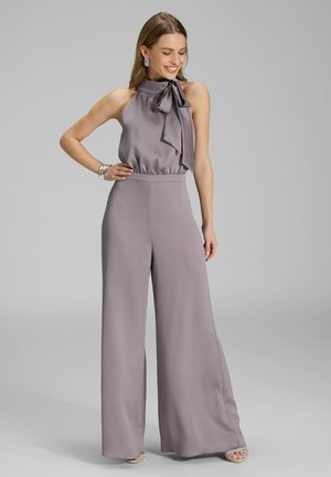 Laventelin jumpsuit leveiden lahkeiden ja halterneck-muotoilun kanssa, jossa on sidottu nauhamainen yksityiskohta kauluksessa ja teksturoitu kangas. Hopeiset asusteet.