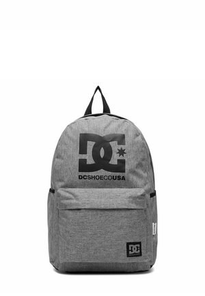 Grå stofrygsæk med sort DC Shoes logo og frontlomme med lynlås, med et topgreb og sideetiket på en hvid baggrund.