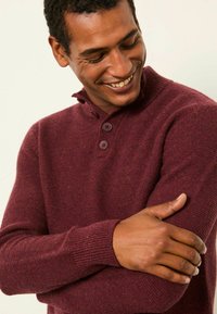 Burgunderroter Strickpullover mit hohem Kragen, einem Knopfverschluss mit drei Knöpfen, gerippten Bündchen und einer weichen Textur mit subtilen Sprenklern.