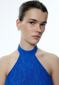 Blaues Spitzen-Haltertop mit hohem Ausschnitt und floralem Muster. Glatte Textur mit freiem Schultern und taillierter Passform.