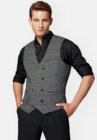 Szary, kratkowany kamizelka z dekoltem w serek, podwójnym zapięciem i kieszeniami z przodu, noszona na czarnej koszuli. Gładka tekstura, dopasowany krój.