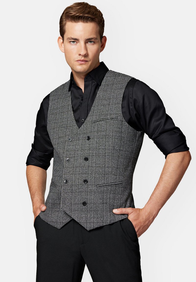 Szary, kratkowany kamizelka z dekoltem w serek, podwójnym zapięciem i kieszeniami z przodu, noszona na czarnej koszuli. Gładka tekstura, dopasowany krój.