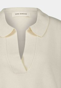 Crème-kleurige gebreide trui met een zachte textuur, voorzien van een korte kraag en een v-hals ontwerp. Het label leest "Sofie Schnoor."