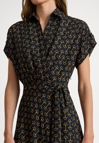 Vestido camisa preto com mangas curtas, apresentando um padrão repetido de guarda-chuvas amarelos, amarrado na cintura para uma silhueta ajustada.