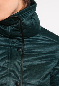 Tyrkysová prošívaná bunda s vysokým límcem, černými patentkami a texturovanou tkaninou se jemným vzorem. Ozdobena černými detaily.