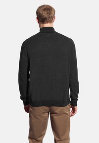 Suéter gris oscuro con cuello alto y mangas largas, con una textura suave. Llevado sobre pantalones marrón claro. Vista trasera visible.
