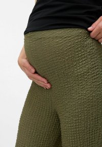 Olive green textured leggings made of a woven material, displaying a crinkled pattern, fitted shape, and elastic waistband.